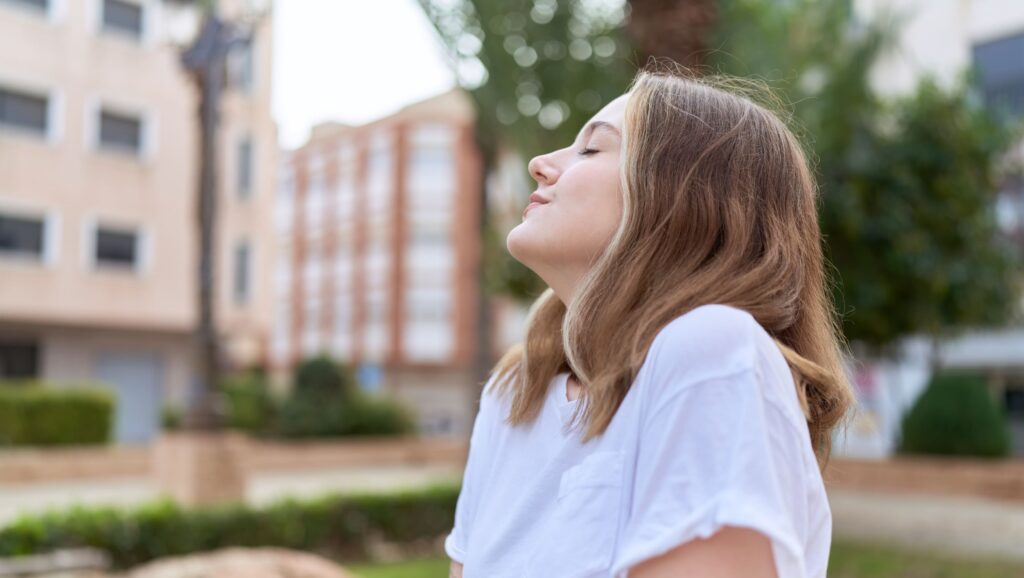 A sober woman standing outdoors with her eyes closed reflecting signs of liver healing and recovery.